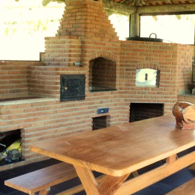 Churrasqueira em tijolo com forno de pizza e mesa de madeira